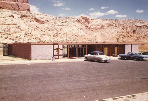 a brick building with 1960s-era vehicles parked in front