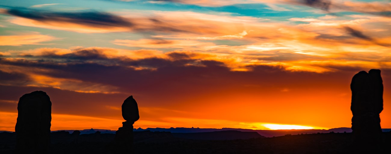 Vibrant orange, black and blue sunset across silhouette of Balanced Rock