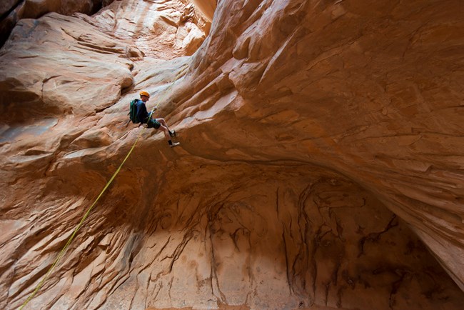 A person canyoneers over a ledge in Fiery Furnace
