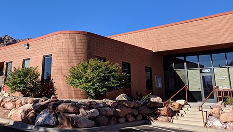 The entrance to a brown brick building with many windows and elaborate stone landscaping.