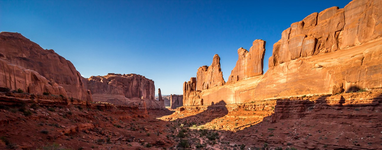 Tall red colored rock walls with a low lying area in between covered in green plants.