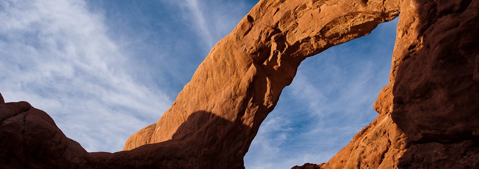 a broad red stone arch with light clouds overhead