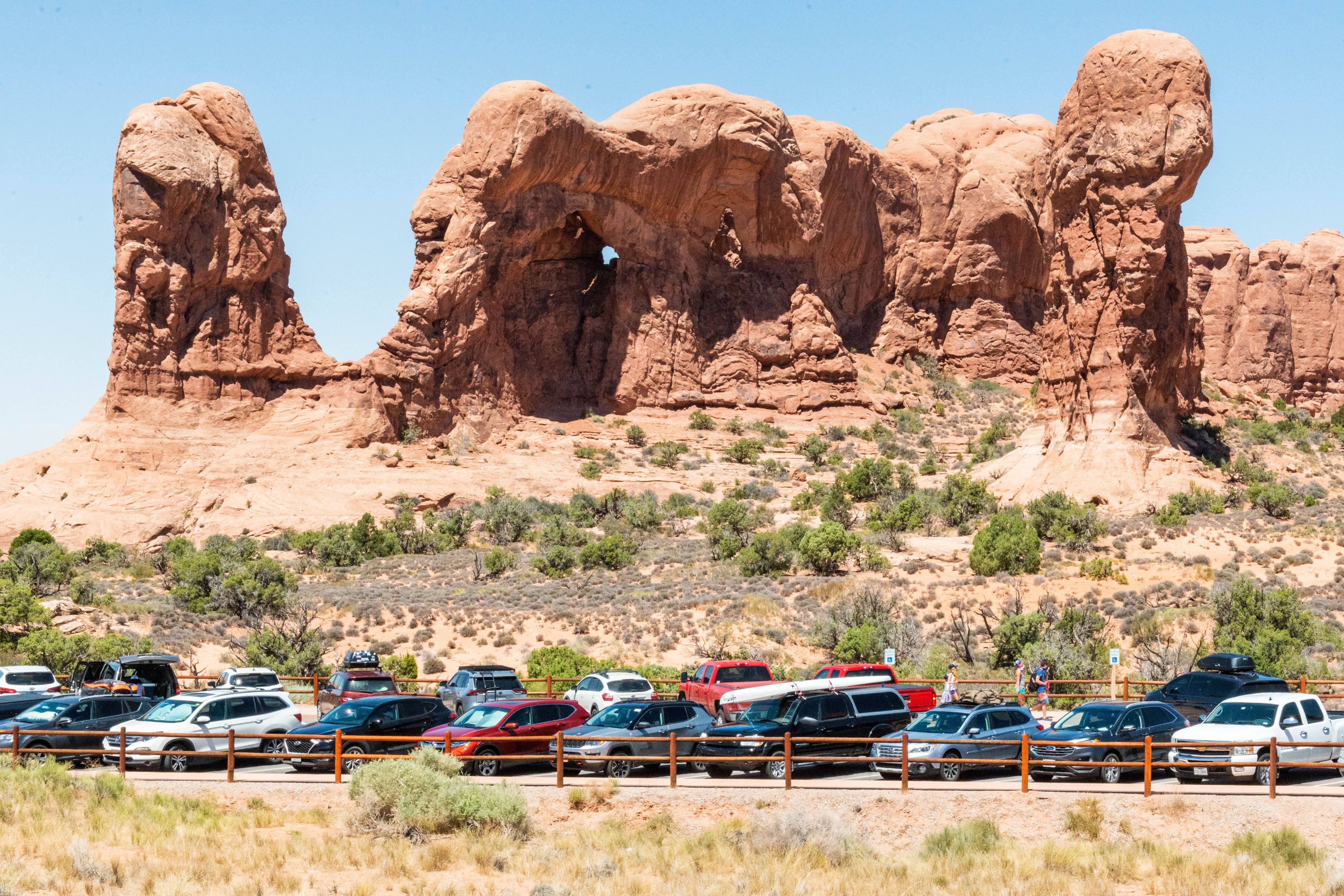 large stone columns and arches loom above vehicles parked along a fence, blue sky above large stone columns and arches loom above vehicles parked along a fence, blue sky above