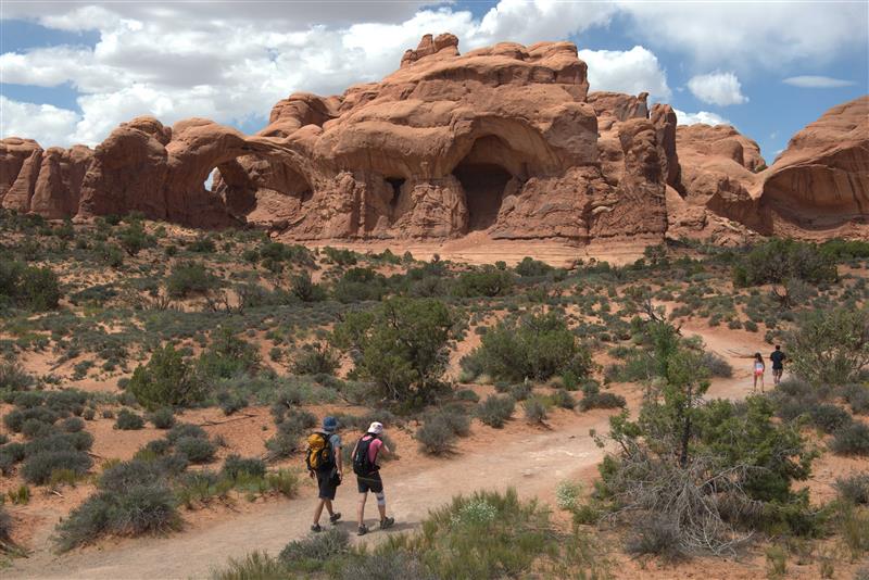 park visitors walk along a trail in front of large sandstone features