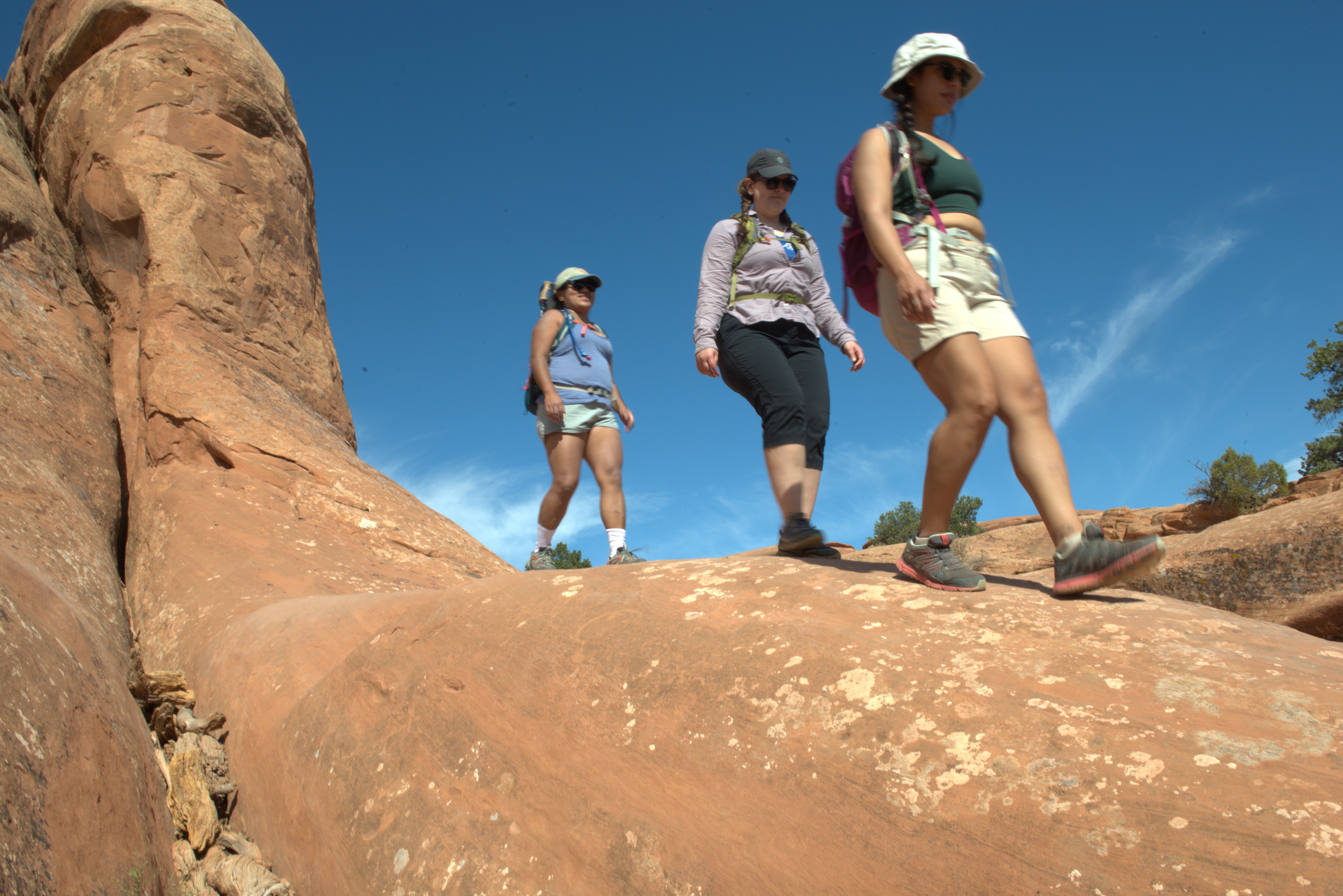 three women hiking on tan sandstone, blue sky in background three women hiking on tan sandstone, blue sky in background