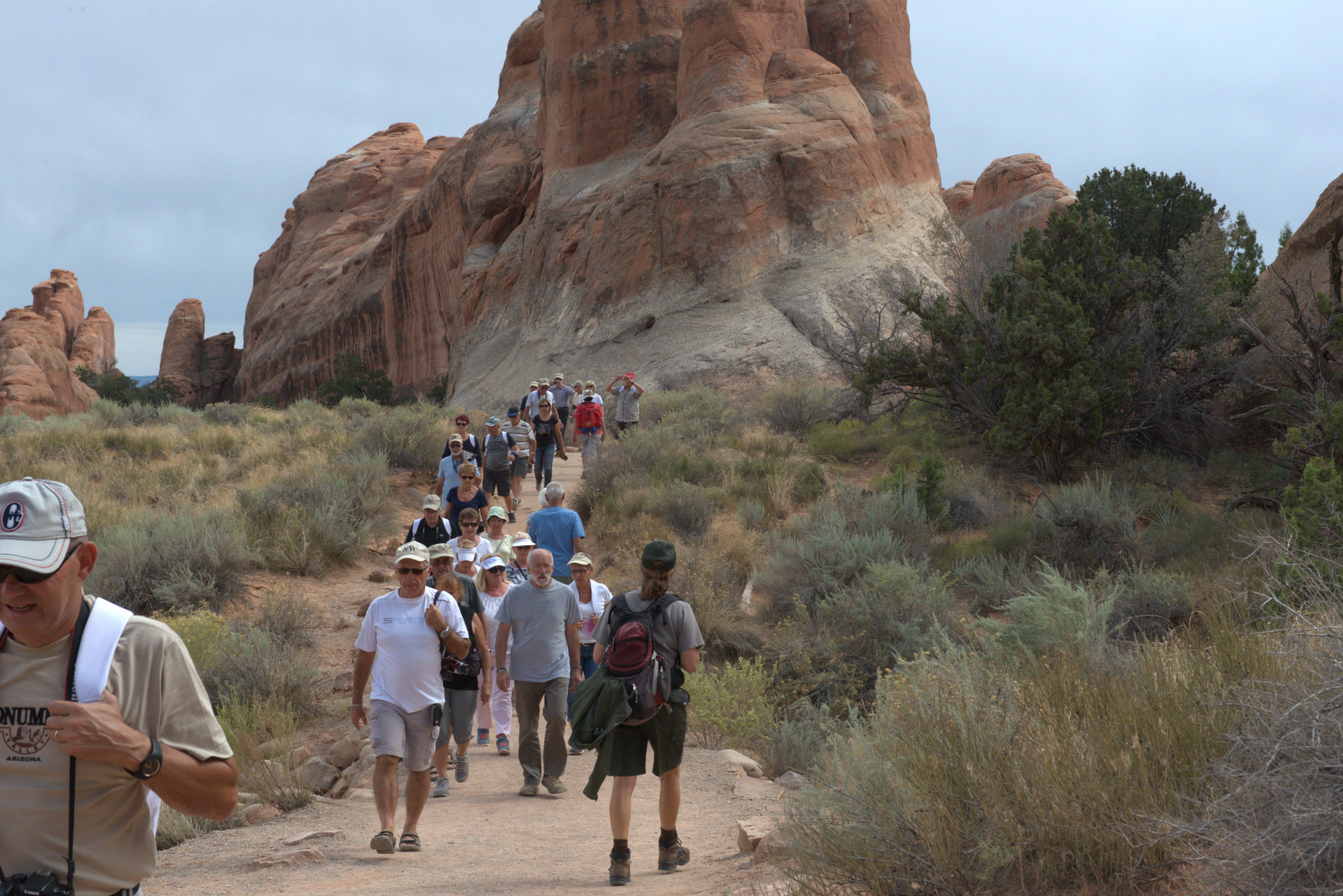Hikers at Devils Garden many people walking on a trail between desert shrubs, red sandstone feature in background
