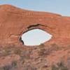 An arch in a red sandstone wall and clear blue skies in the distance.