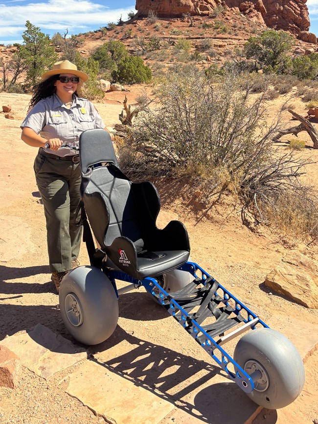 park ranger pushes an unoccupied all-terrain wheelchair on dirt trail