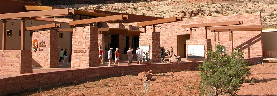 people look at exhibits mounted on red stone walls outside a reddish stone building people look at exhibits mounted on red stone walls outside a reddish stone building