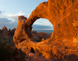 Standing tall, this red rock is illuminated by the sun and has a perfectly cut circle in it, and through the O shape you can see across the red rock landscape.