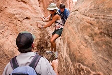 Visitors navigate through a thin gap in the rock while a ranger waits.