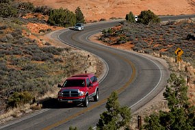 vehicles driving on a curving road through red rock and green vegetation
