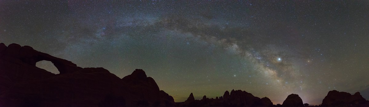 A large arch appears black against the night sky. The milky way appears like an arching band of stars.