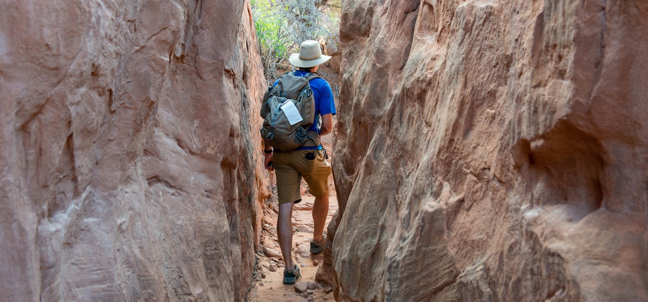 A hiker walks between two tall sandstone rock walls