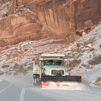a snowplow on a snowy road with tall red rock cliffs