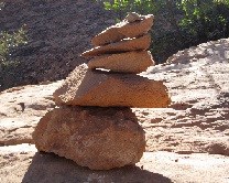 A stack of rocks creating a cairn A stack of 5 orange colored rocks in various sizes. The stack creates a half a foot pile and sits on exposed hard rock.