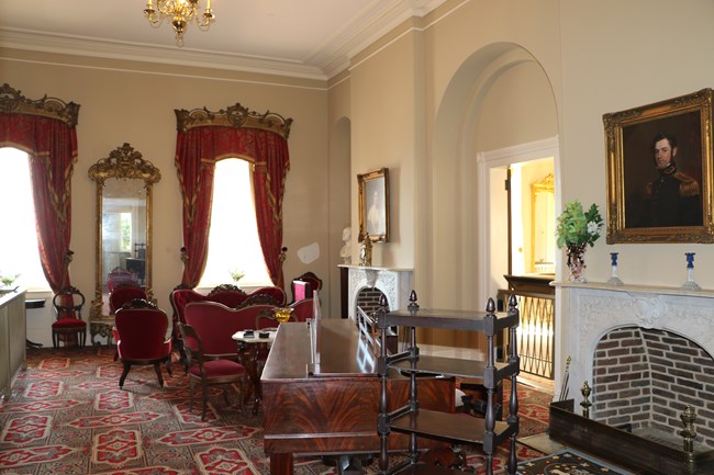 A white parlor with red furniture and paintings on the wall.