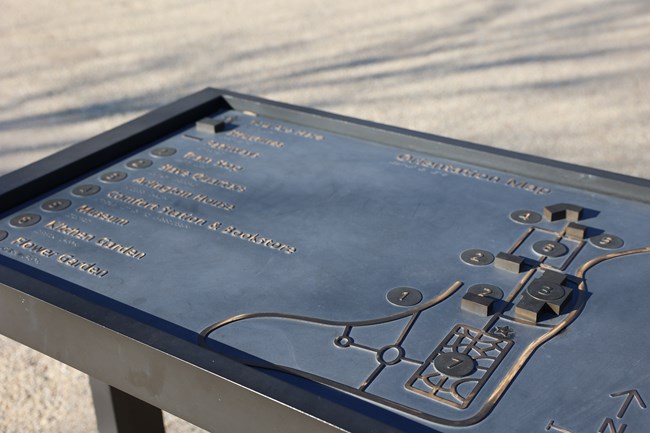 A metal relief orientation map with buildings, sidewalks, and braille labels.