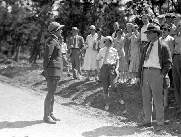 Polly Mead in her NPS uniform stands on a dirt road addressing a group of visitors.