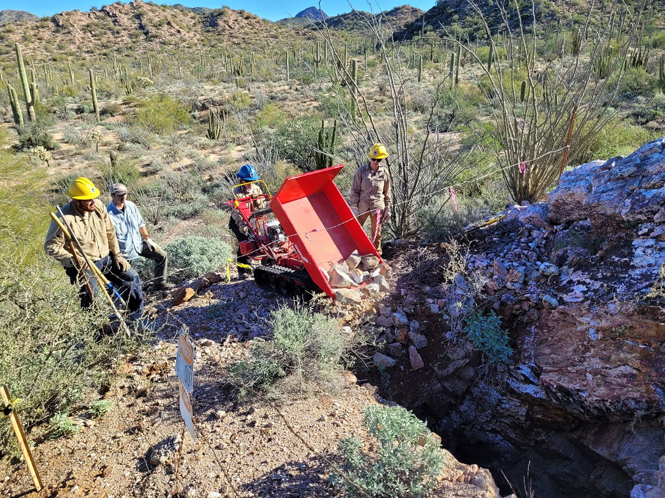 Senita Basin Mine a group of people in hard hats use a machine to move rocks into an abandoned mine