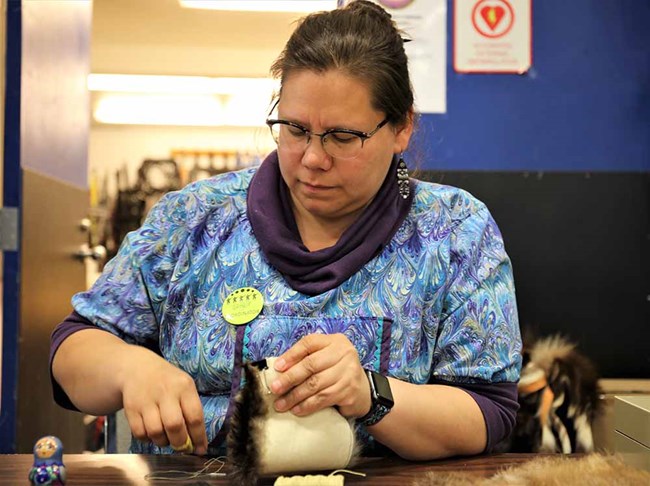 A woman sews beaver fur into clothing. A woman works with fur to sew a garment.