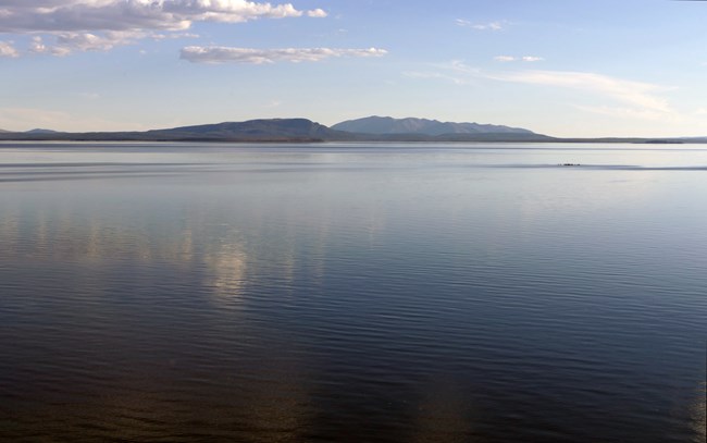 Photo looking out towards a lake. The water is blue with mountains in the background.
