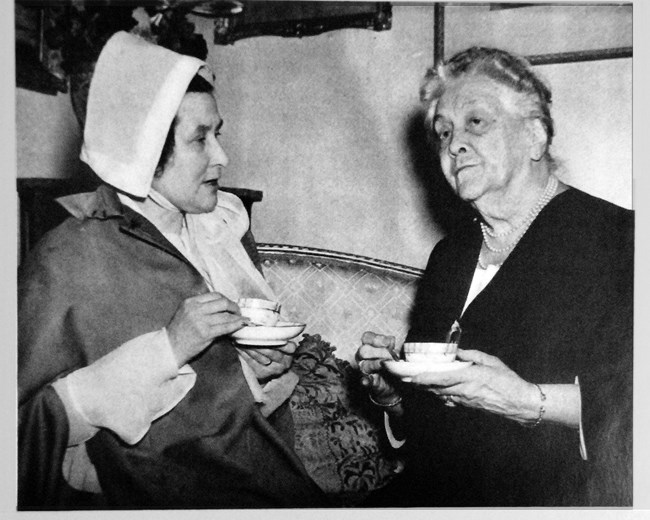 Two women seated, one dressed in historic clothes, the other holding tea cup