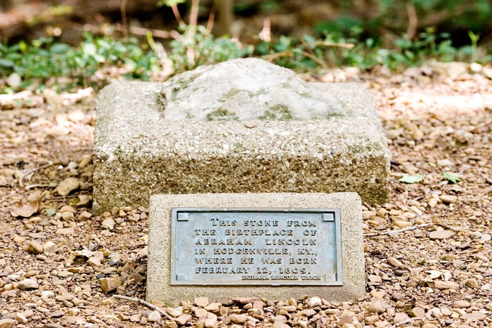 Stone on concrete slab, bronze plaque in front reads This stone from the birthplace of Abraham Lincoln in Hodgenville, KY, where he was born February 12, 1809.