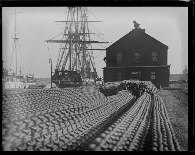 Rows of anchor chain in the foreground with Building 10 and USS Constitution in the background.