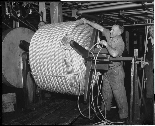 Navy Yard worker in the ropewalk with rope used for a ship wrapped on a large spool.