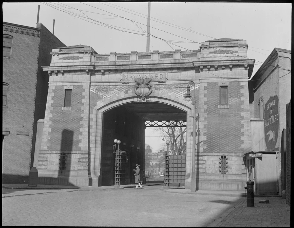 08_06_016902 - Entrance to Charlestown Navy Yard Black and white photograph of a large brick archway with a marine guard marching past the opening.