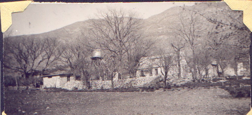 A black and white phto of a ranch compound inside a stone fence