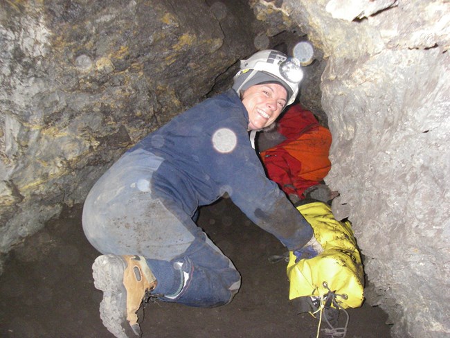 A staff member getting ready to head into a crawl inside of a cave
