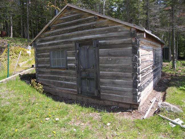 Historic wood shack with door and window, grass in front.