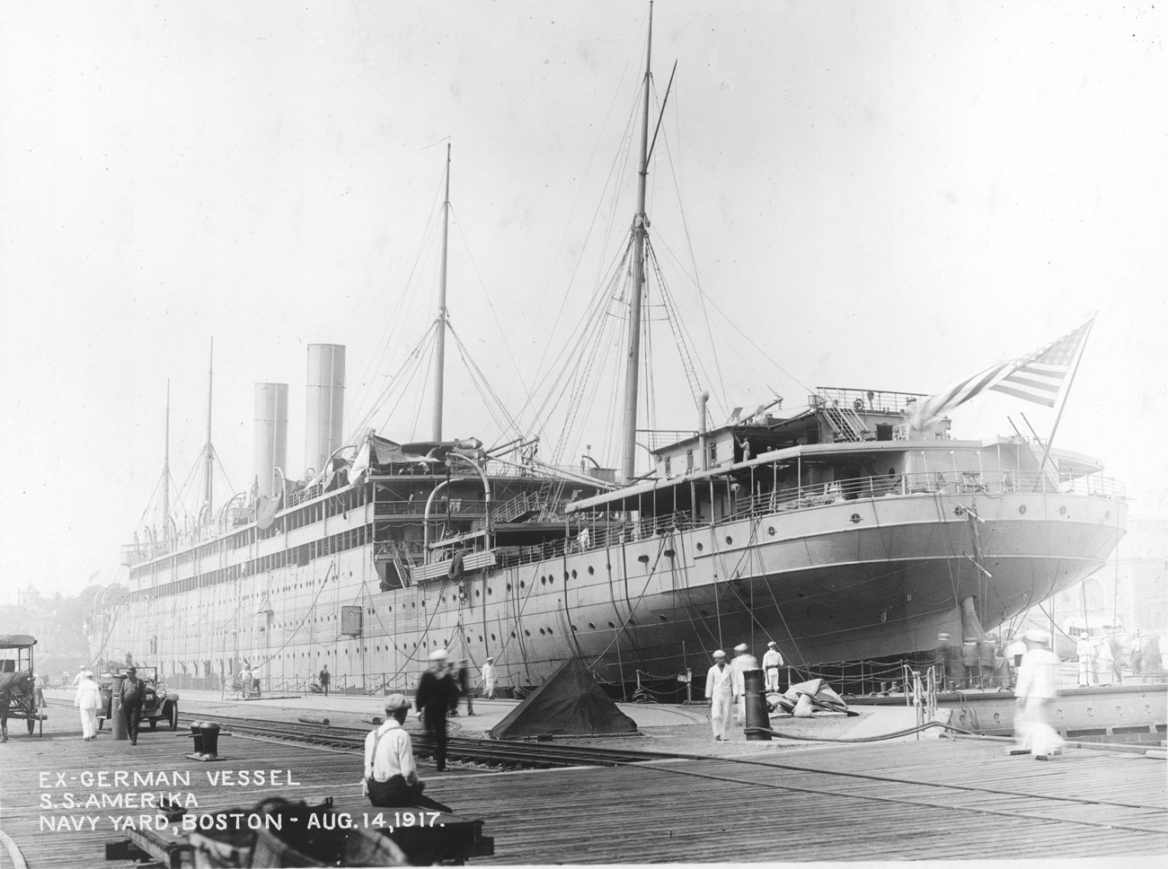 A large ocean liner under construction at a navy yard with ropes hanging off its sides.