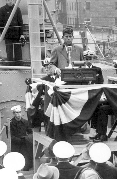 a young JFK speaking from behind a podium.