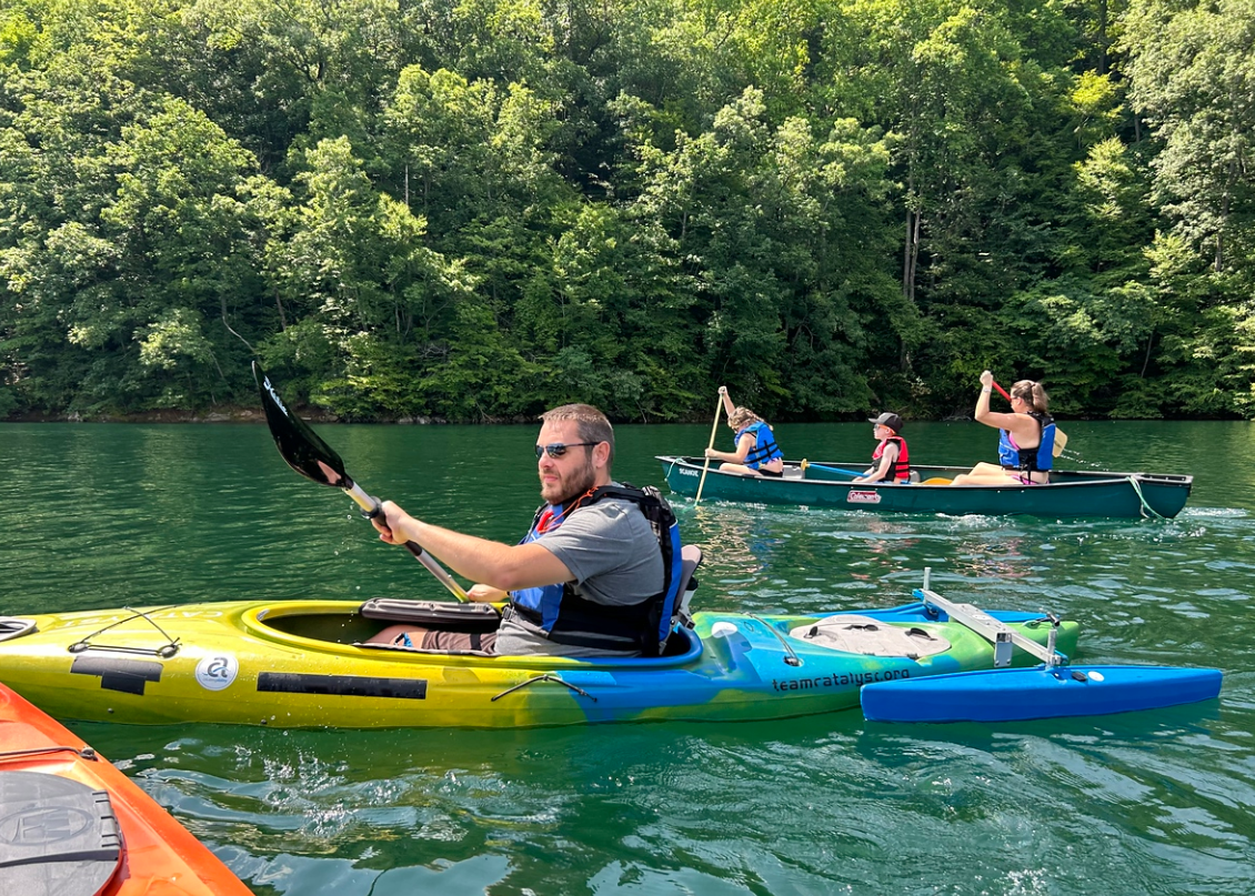 A kayaker in an adaptive kayak paddling with others in kayaks nearby.