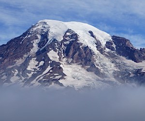 A glaciated mountain peak rising above a layer of clouds.