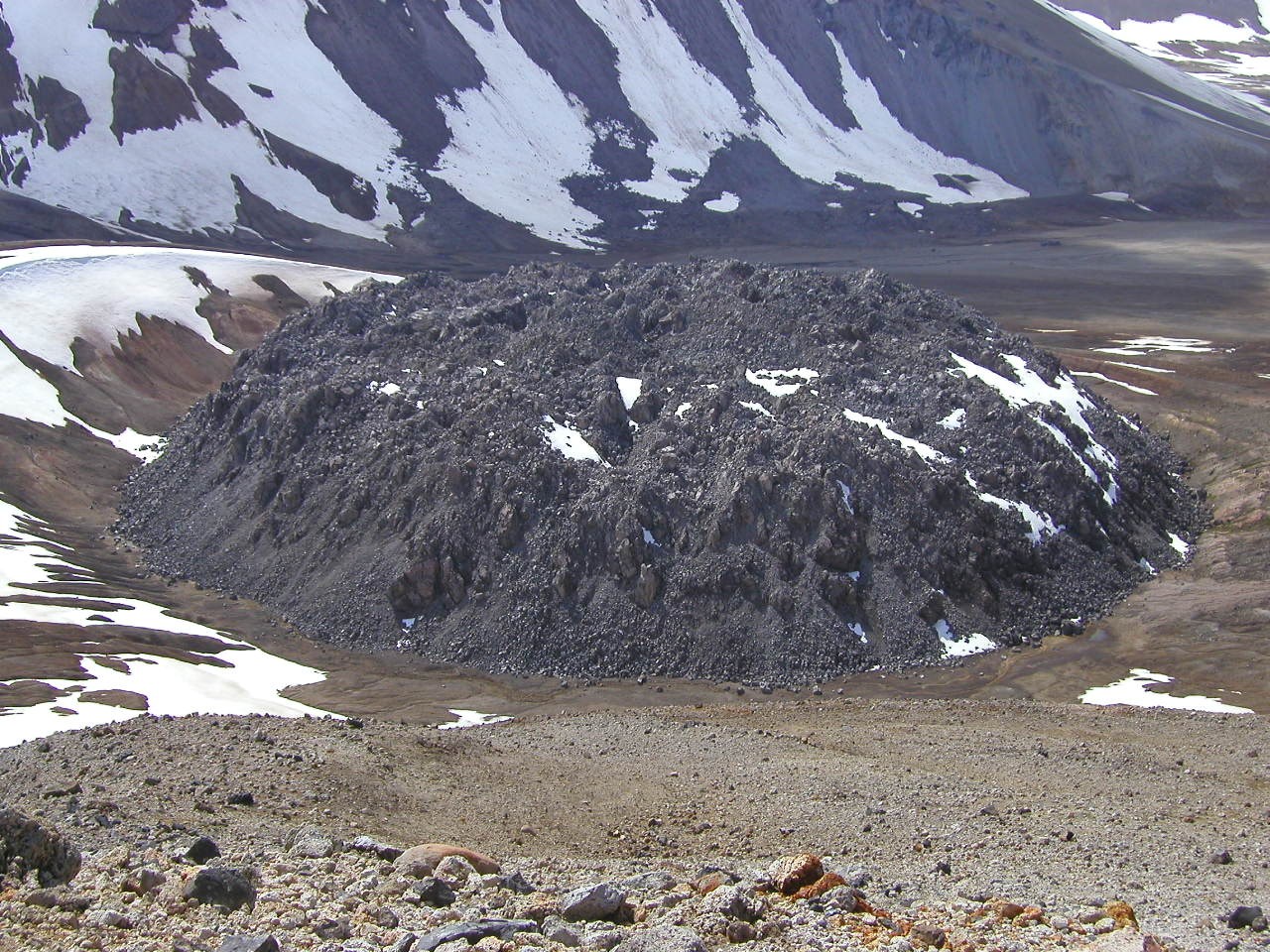 dome-shaped rock hill with partial snow cover on surrounding volcanic landscape