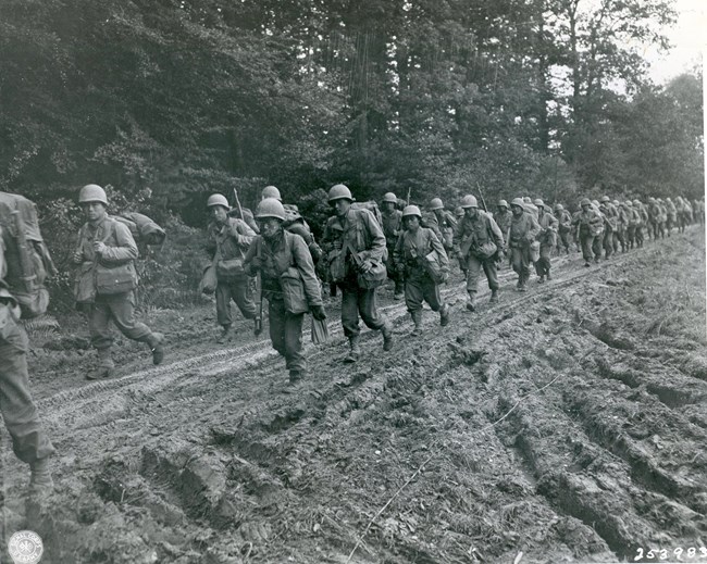 111-SC-253983 Men in military uniforms marching down a muddy road