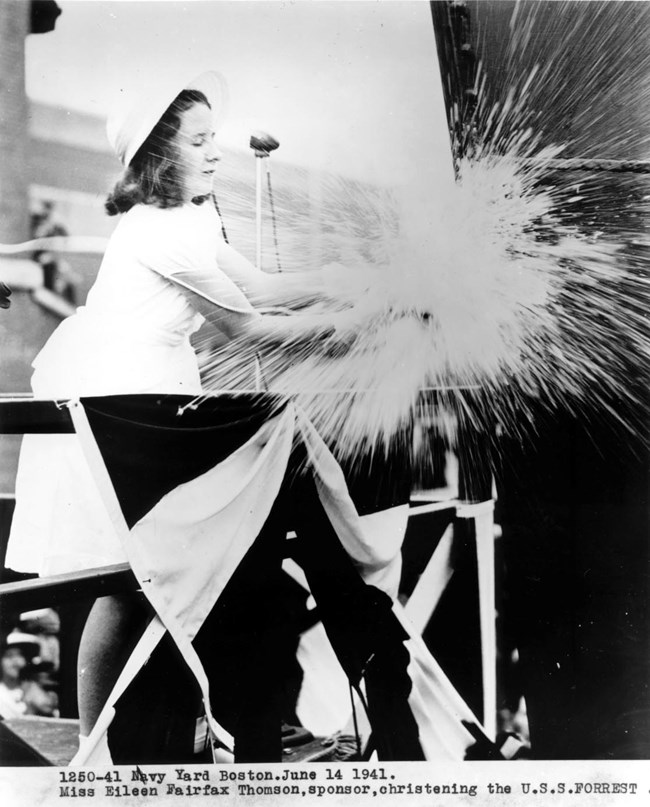 A young woman christening a ship by smashing a bottle onto it.