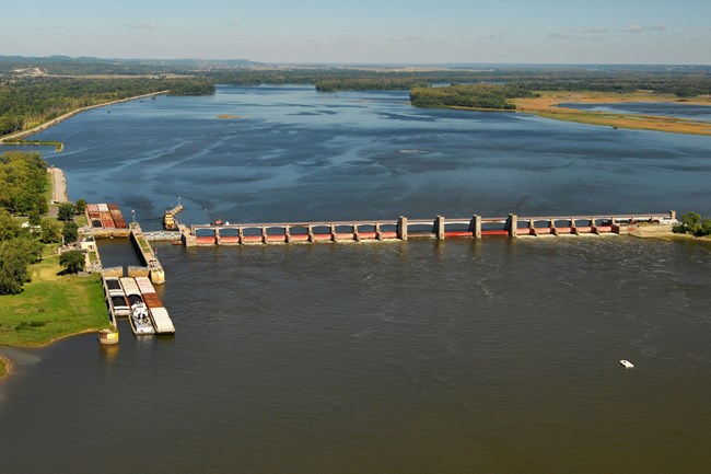 Color photograph of barge locking facility and a dam stretching across the Mississippi River.
