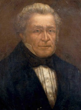A painted portrait of Carlos Dehault Delassus – a middle-aged man with gray hair, wearing a black coat, black bow tie, and a pleated, high-collared white shirt.