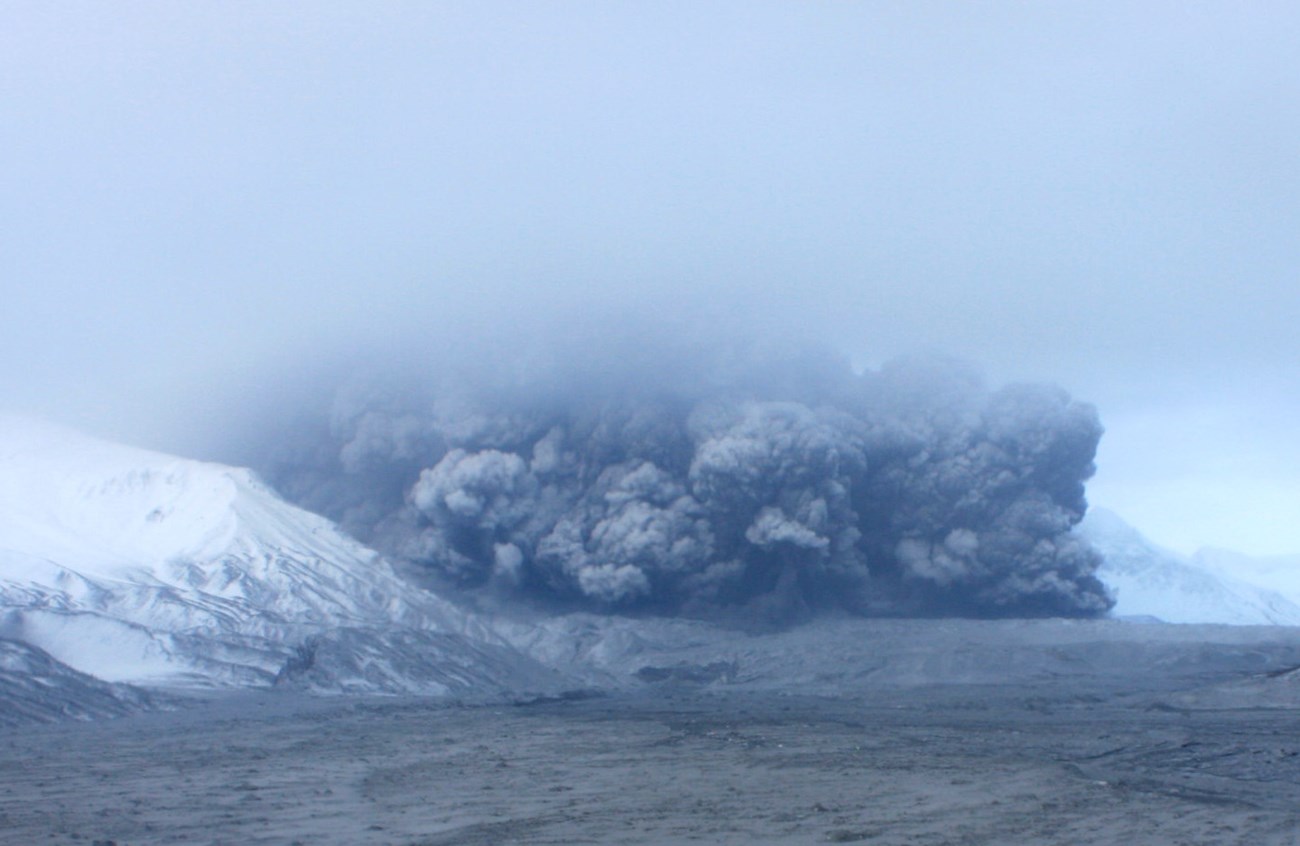 photo of a dust and ash cloud moving down a treeless u-shaped valley