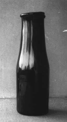 A black and white photo of a dark-glass bottle.  It is tall with a slightly irregular shaped neck.