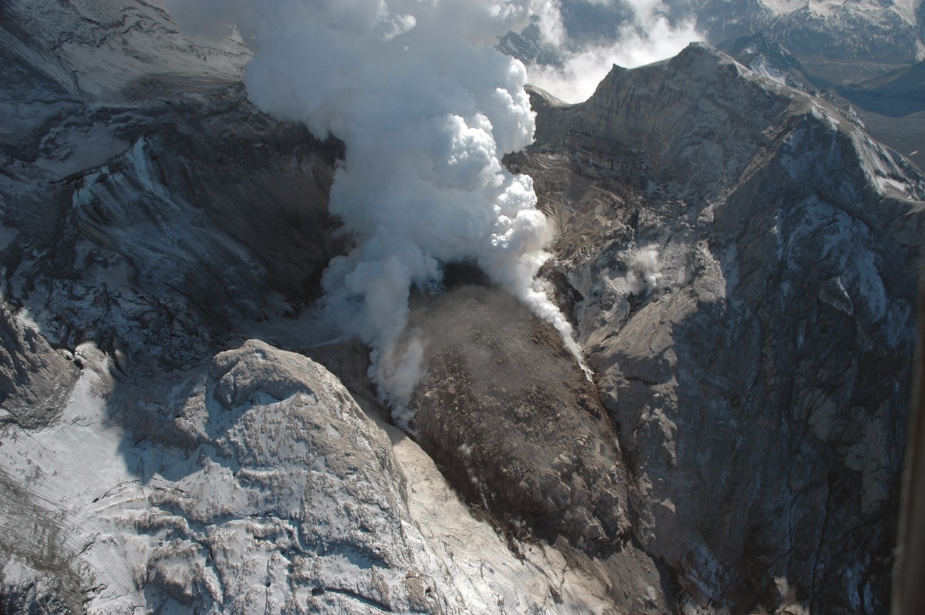 photo of a dome-shaped hill and steam cloud in a mountain top volcanic crater