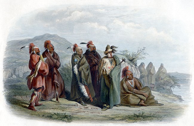 1294 Bodmer’s painting shows five standing and one seated Sauk/Fox men with painted faces, wrapped in large robes. They are near a river with a hill behind them.