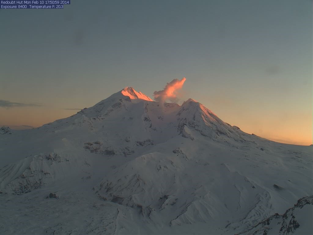 snow covered volcanic peak with steam plume above its summit crater.