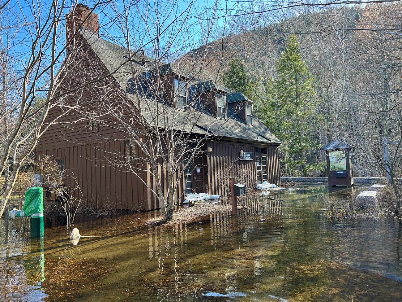 Great Meadow Nature Center Brown building with sandbags in front of its two sets of doors, surrounded by water.