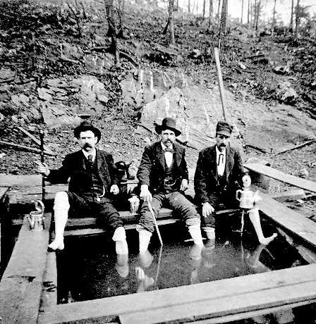 Three men soaking feet in dugout pool